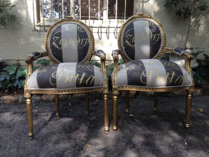 A Pair of French Style Arm Chairs Hand Gilded With Gold Leaf And Upholstered In an Imported Script Fabric