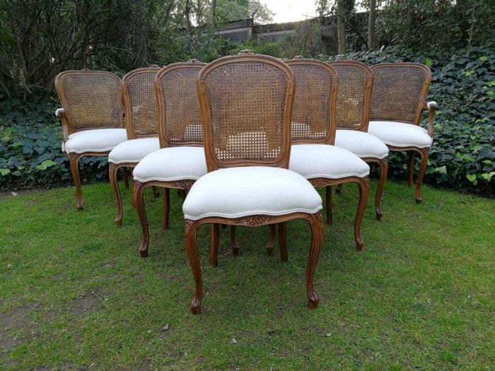 A 20th Century French Set Of Ten Walnut And Rattan Dining Chairs Consisting Of Two Carvers And Eight Dining Chairs Upholstered In A Off-White Linen