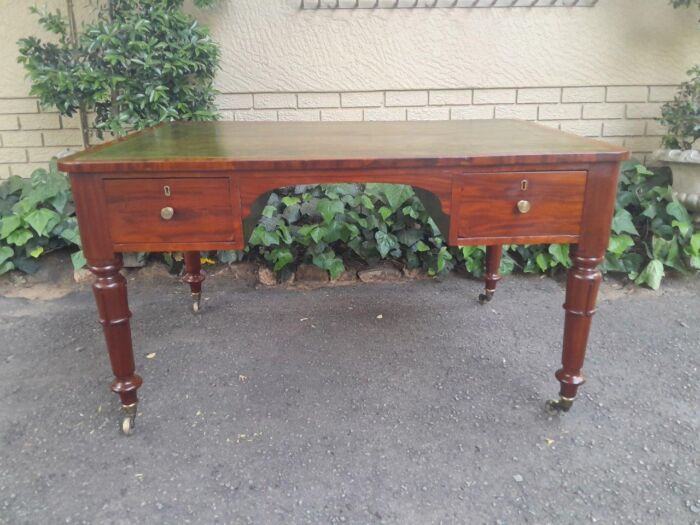 A 20th Century First Half Victorian-Style Mahogany Writing Table With Green Gilt-Tooled Leather Writing Surface With Drawers And Bras Escutcheons (Each Side Panel Fitted With A Secret Drawer) On Large Brass Castors