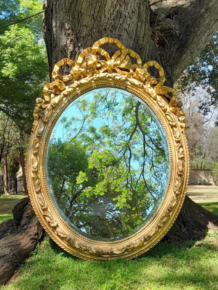 A French Rococo Style Ornately Carved and Gilded Oval Bevelled Mirror